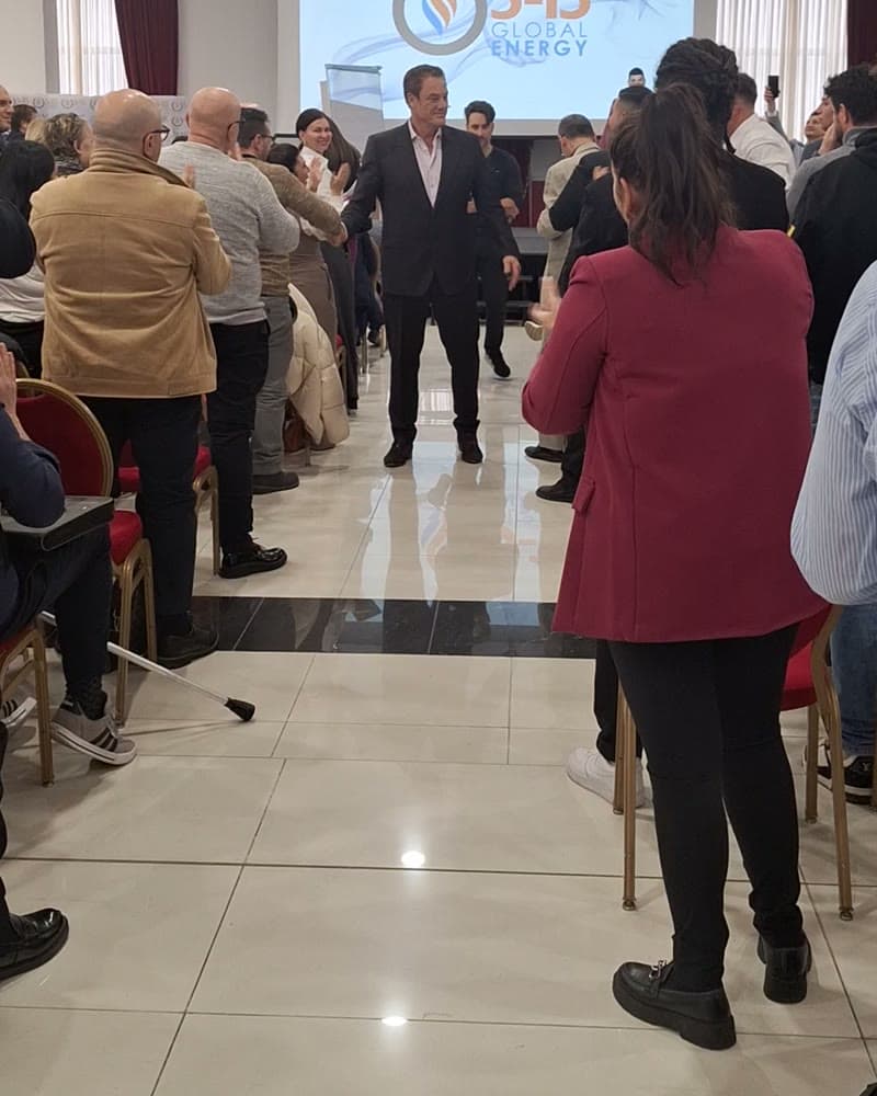 Tom Cummins walking the center aisle of a packed seminar room as attendees stand and applaud