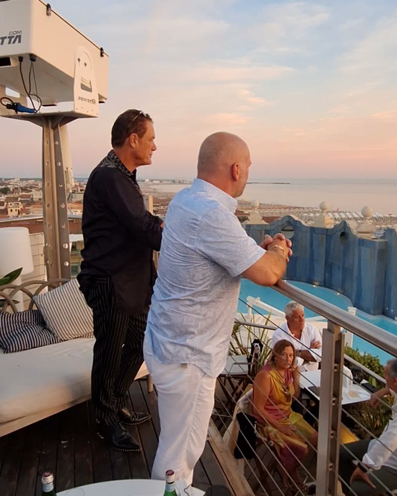 Tom Cummins in conversation on a rooftop terrace above the coastline at dusk