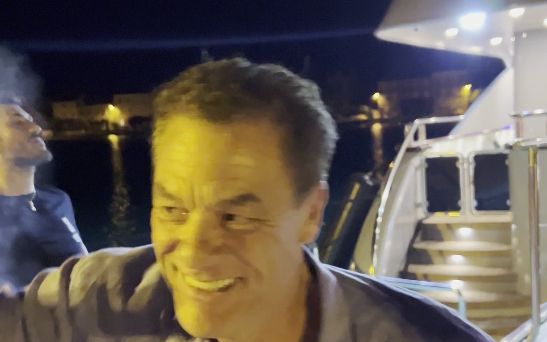 Tom Cummins smiling on a marina dock at night beside a lit superyacht.