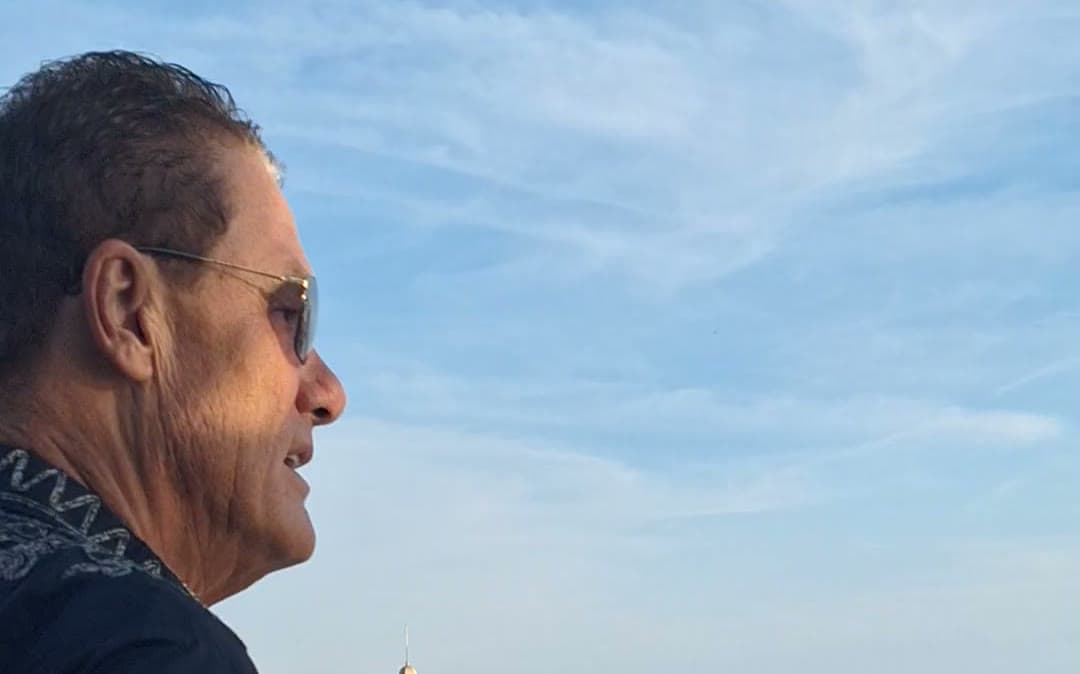 Tom Cummins gazing out over the sea from a rooftop pool deck.