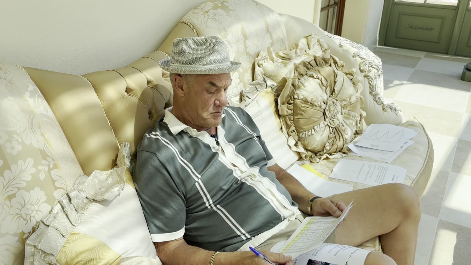 Tom Cummins reading reports on an ornate sofa in his sunlit villa.