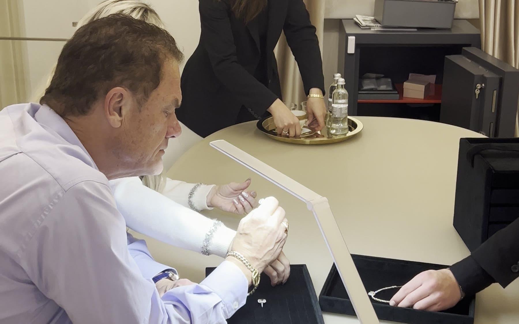 Tom Cummins in white gloves examining a piece under the lamp at a private salon.