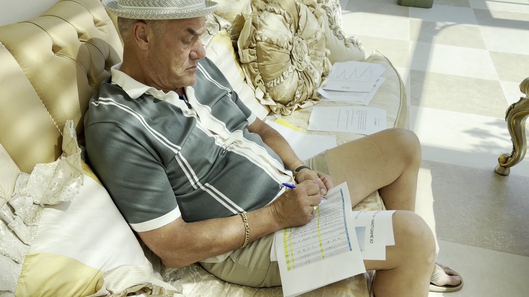 Tom Cummins reading reports with a pen in hand on the villa sofa.