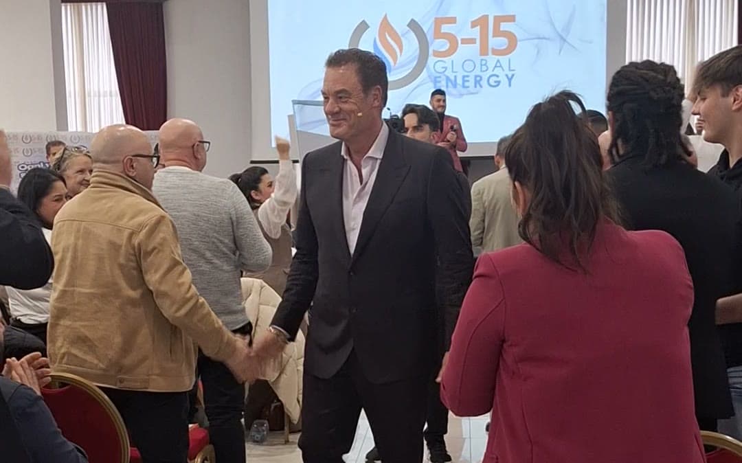 Tom Cummins shakes hands with an attendee in the aisle of a crowded conference hall.