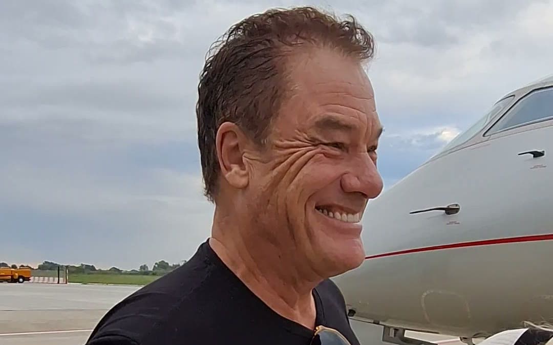 Tom Cummins smiling on the tarmac beside a private jet before boarding.