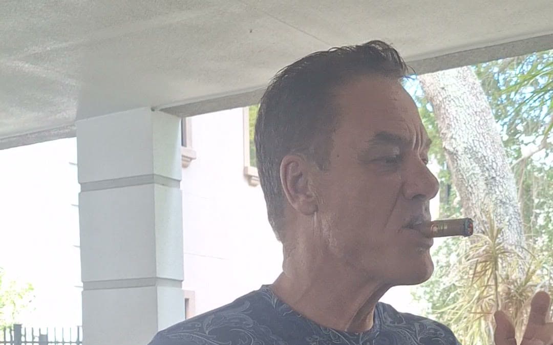Tom Cummins with a cigar in profile on a quiet porch.