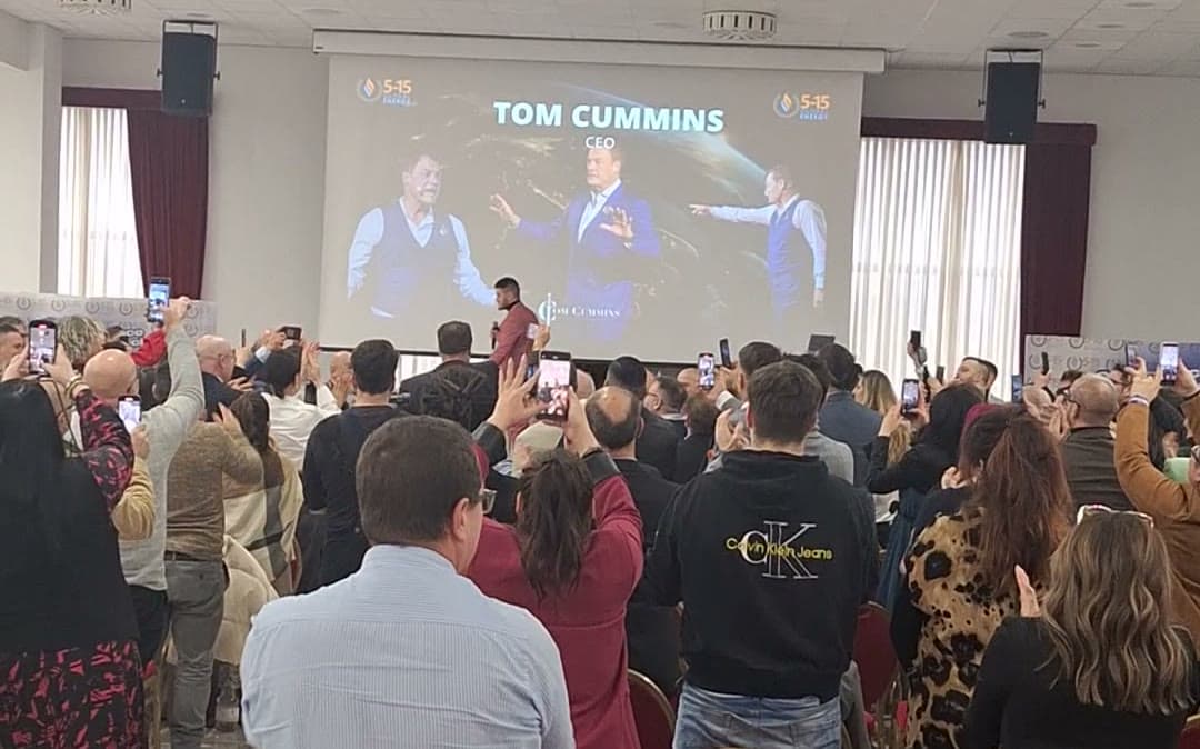 A packed hall on its feet filming as Tom Cummins name fills the screen.