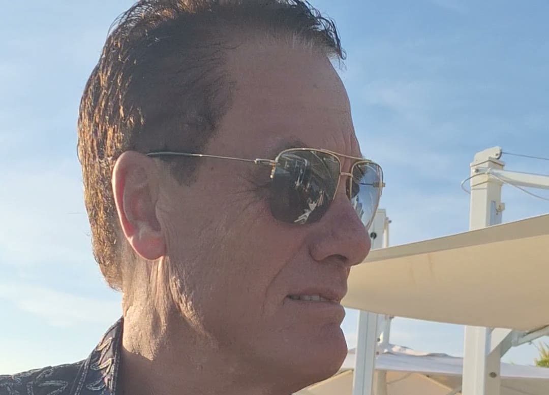 Tom Cummins in sunglasses facing the camera at a seaside seminar venue.