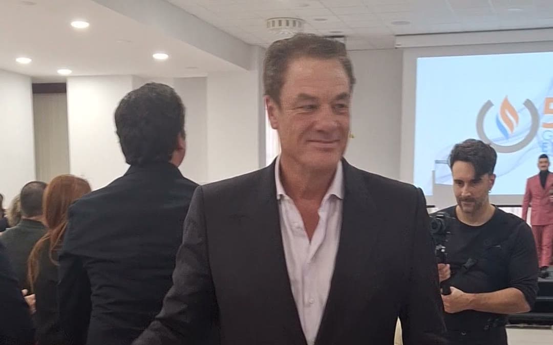 Tom Cummins smiling in a dark suit as he greets attendees in the aisle of a crowded event hall.
