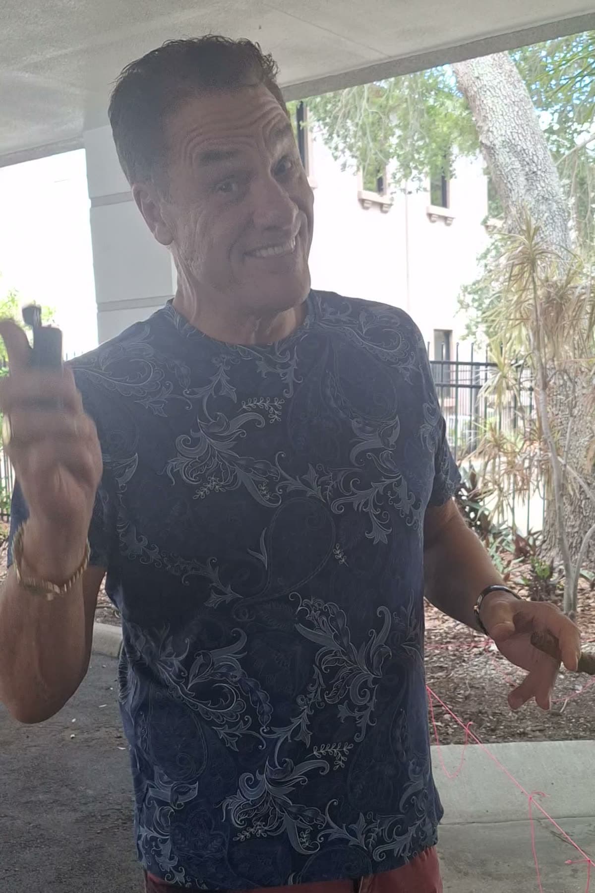 Tom Cummins grinning mid-story on his deck, hands up, in a blue paisley tee