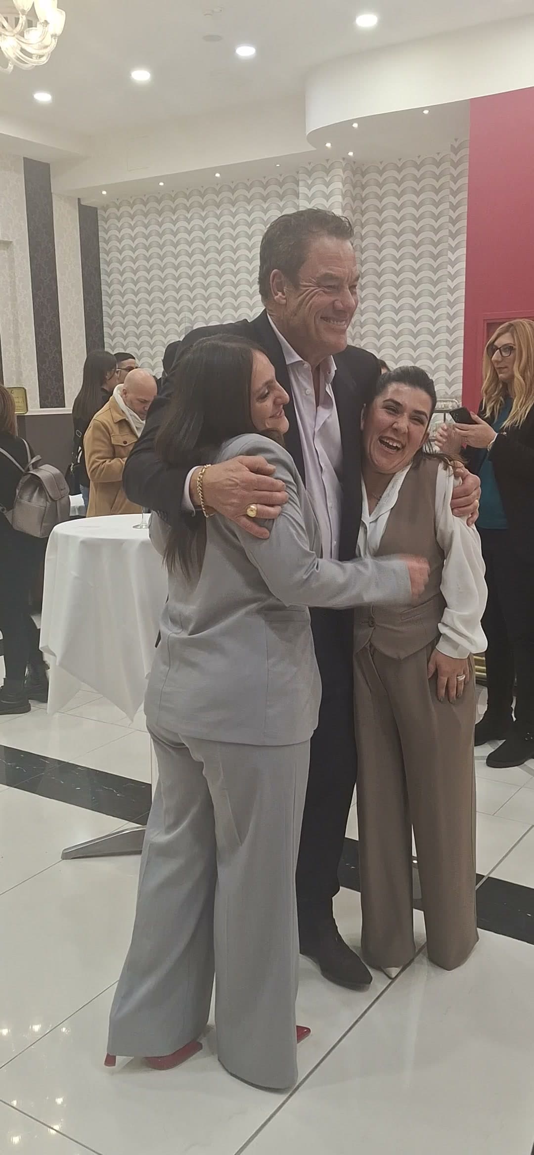 Tom embracing a colleague while friends look on, smiling