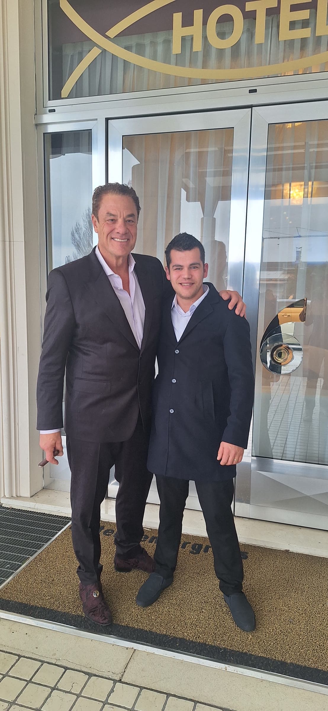 Tom, cigar in hand, with his arm around a young colleague outside a hotel entrance