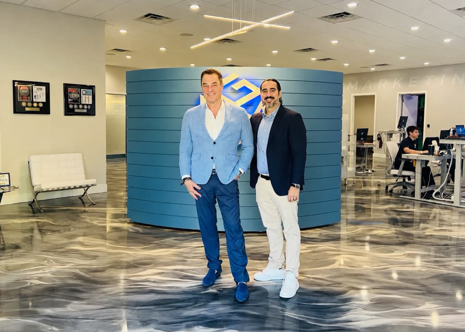 Tom Cummins with Manuel Suarez at the Attention Grabbing Media office, the AGM logo behind them