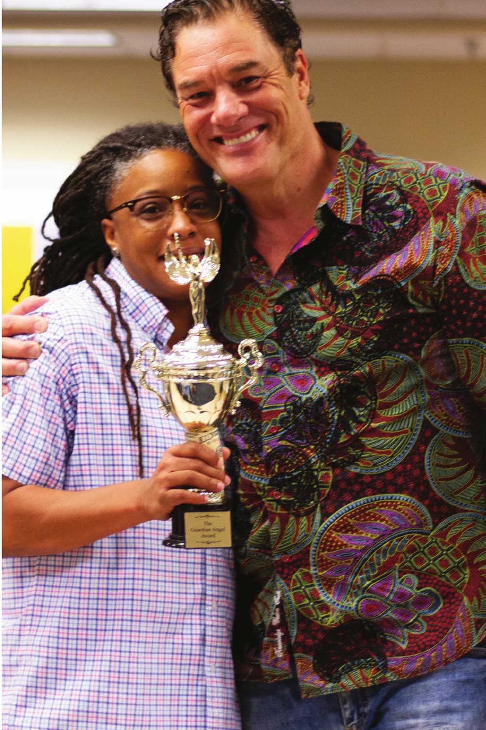 Tom hugging a team member holding the Guardian Angel Award trophy, both beaming