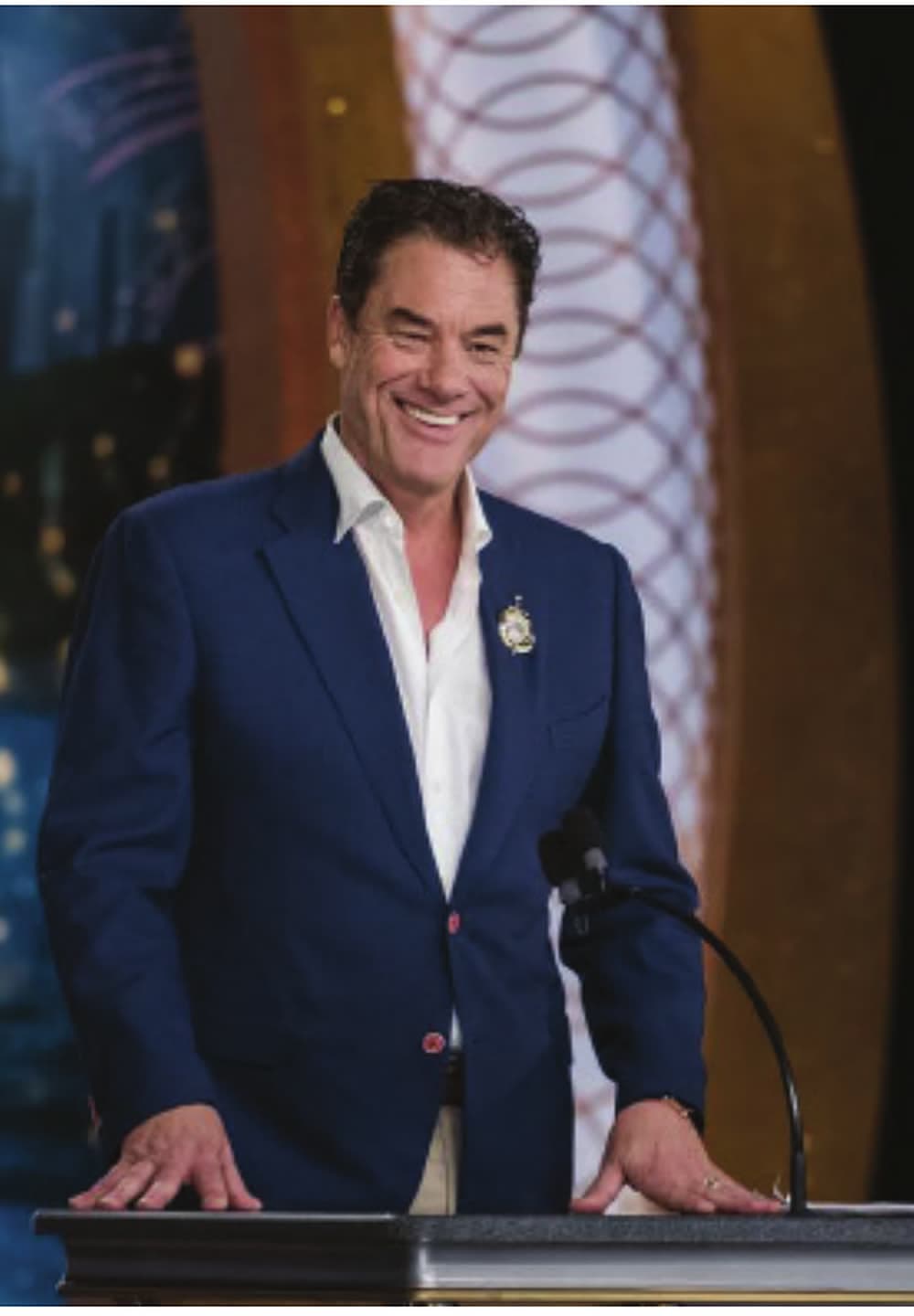 Tom smiling at an ornate gala podium in a navy blazer