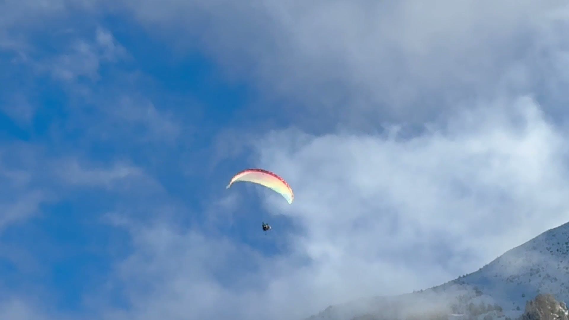 A paraglider drifting past a snow-covered ridge in the Alps