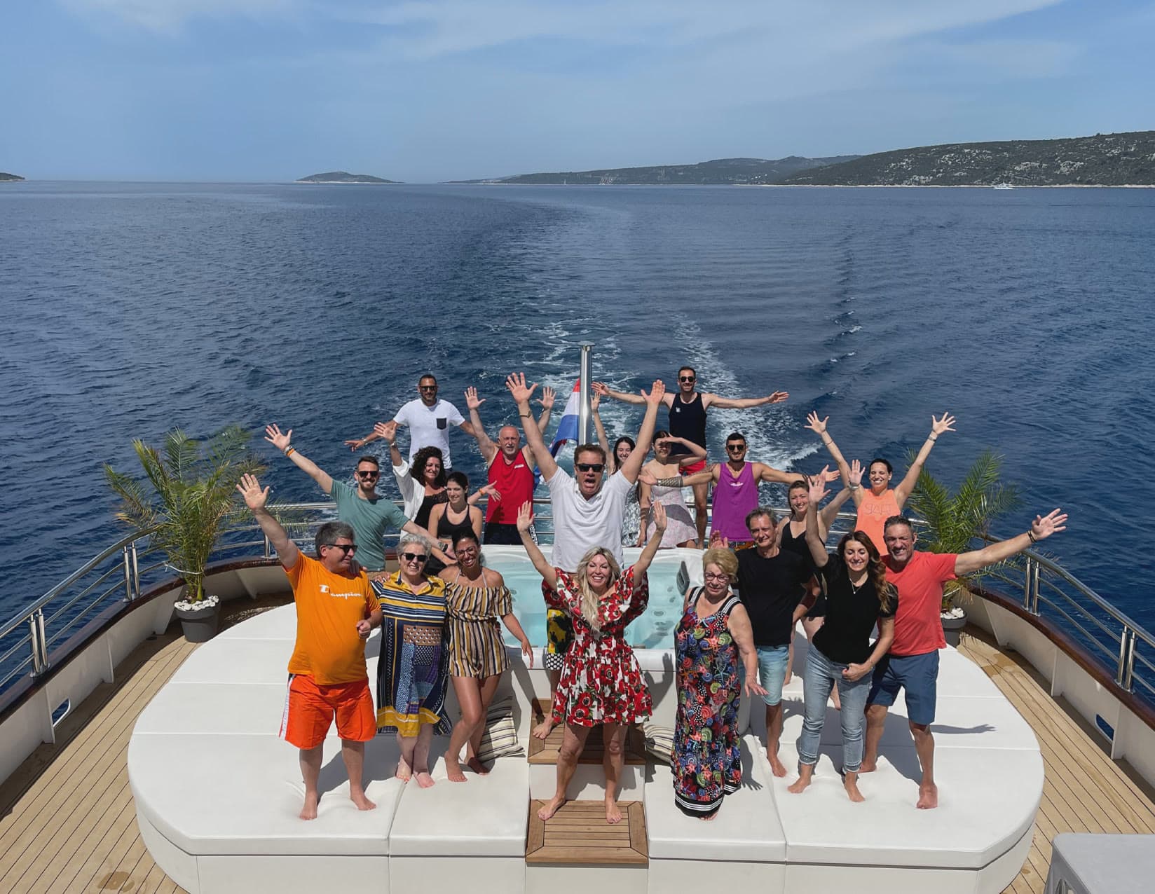 The whole group celebrating with arms raised on a yacht’s aft deck at open sea
