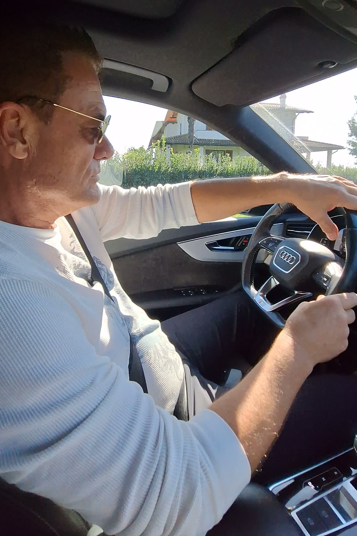 Tom in sunglasses driving through the Tuscan countryside, morning light through the windshield