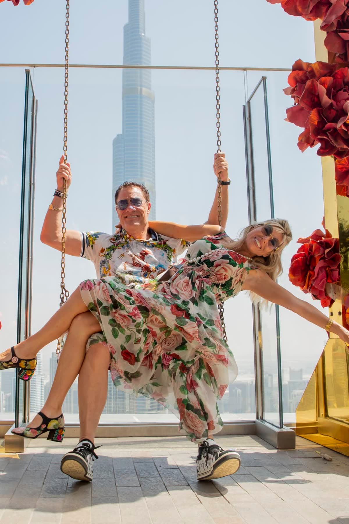 Tom and Victoria laughing on a flower swing in Dubai, the Burj Khalifa behind them