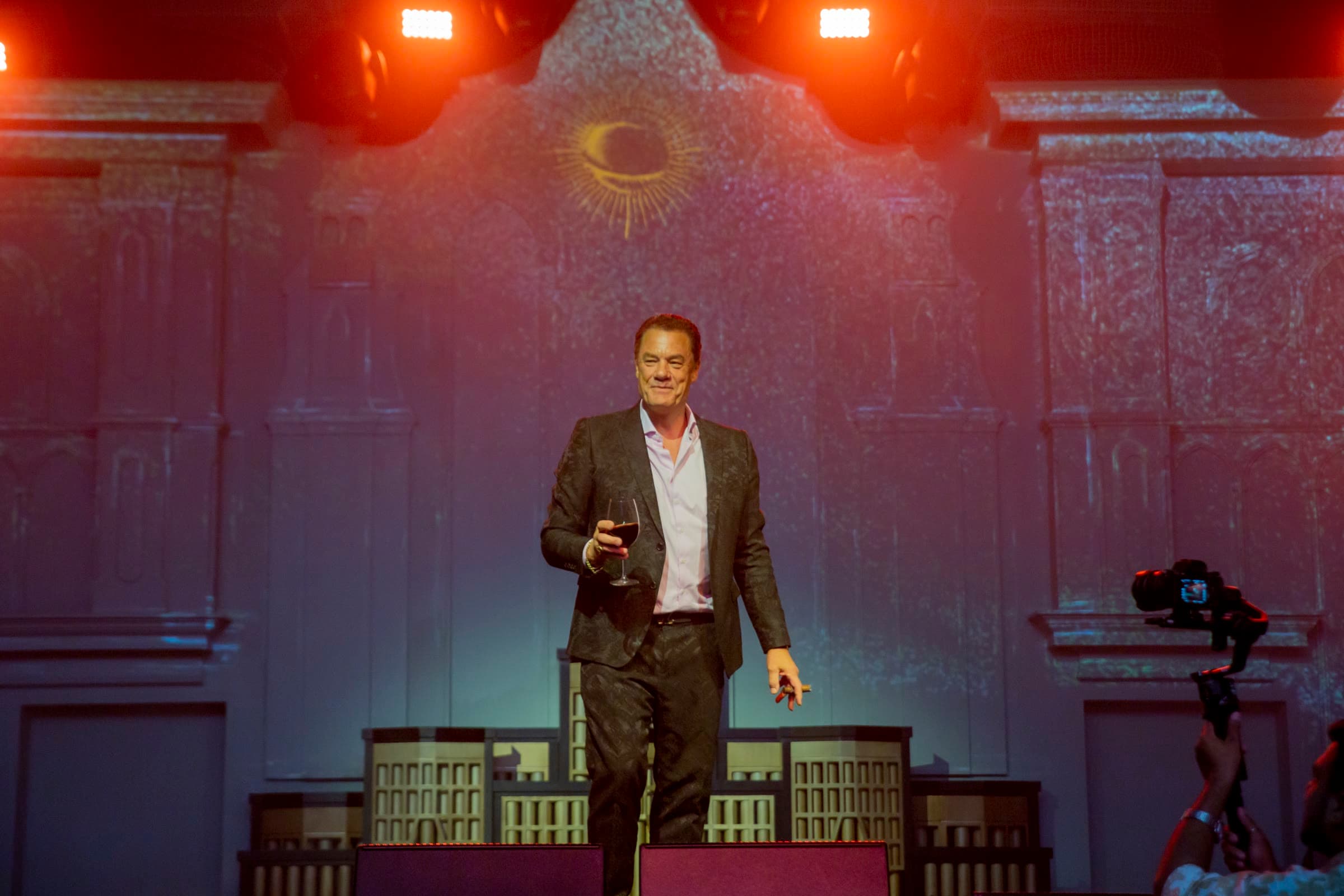 Tom raising a glass on stage under theatrical lights